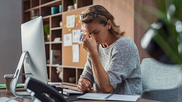 Business woman holding her head when at an office desk